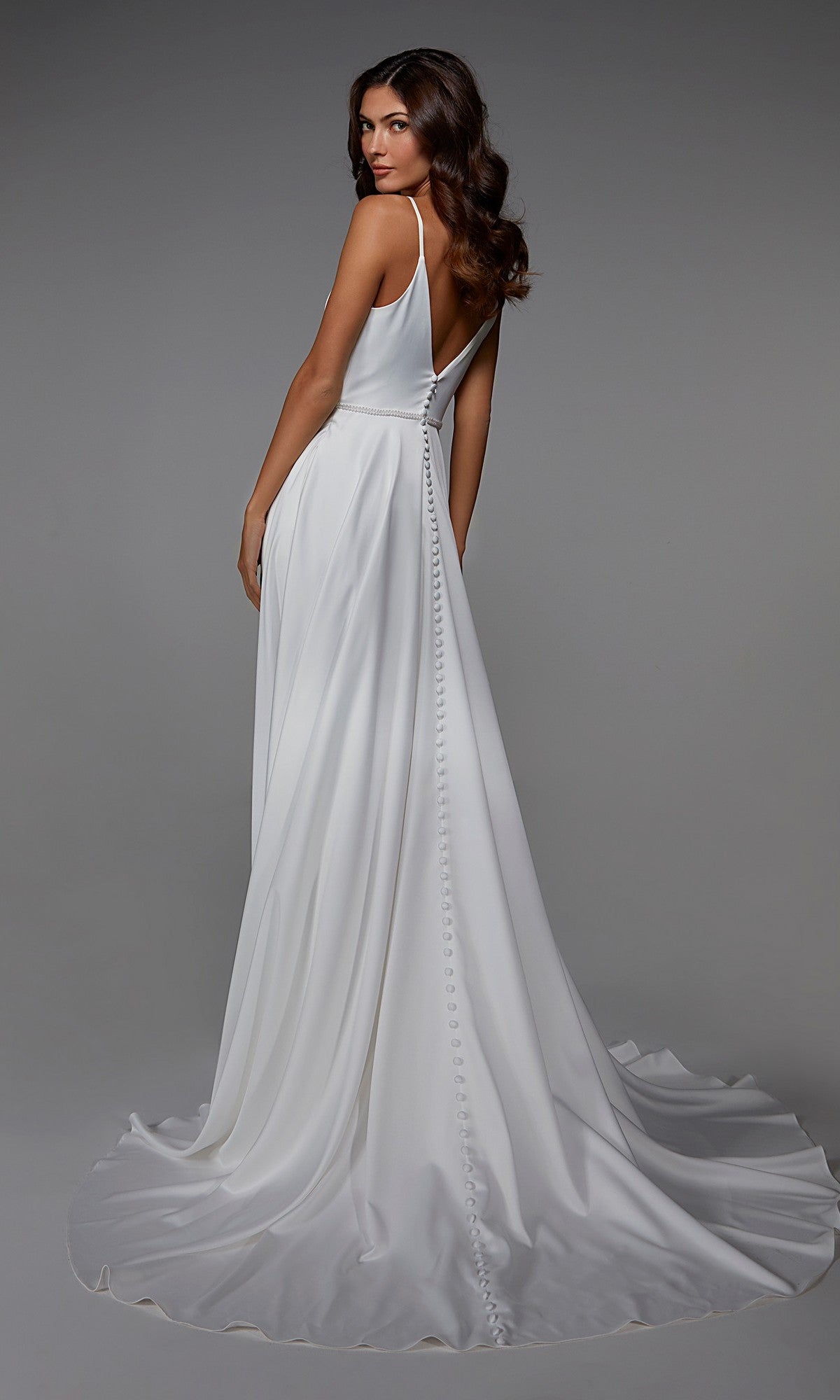 A woman models the Alyce 7024, a sleeveless white satin floor-length formal dress with an A-line skirt, deep V-back, and button detail, standing against a neutral background.
